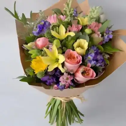 A hand-tied bouquet with lilies and roses arranged with lush green foliage in a stylish wrap.