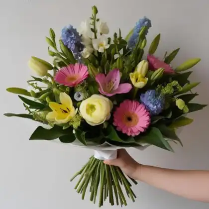 A vibrant gerbera and lily bouquet arranged with fresh greenery in a decorative wrap.